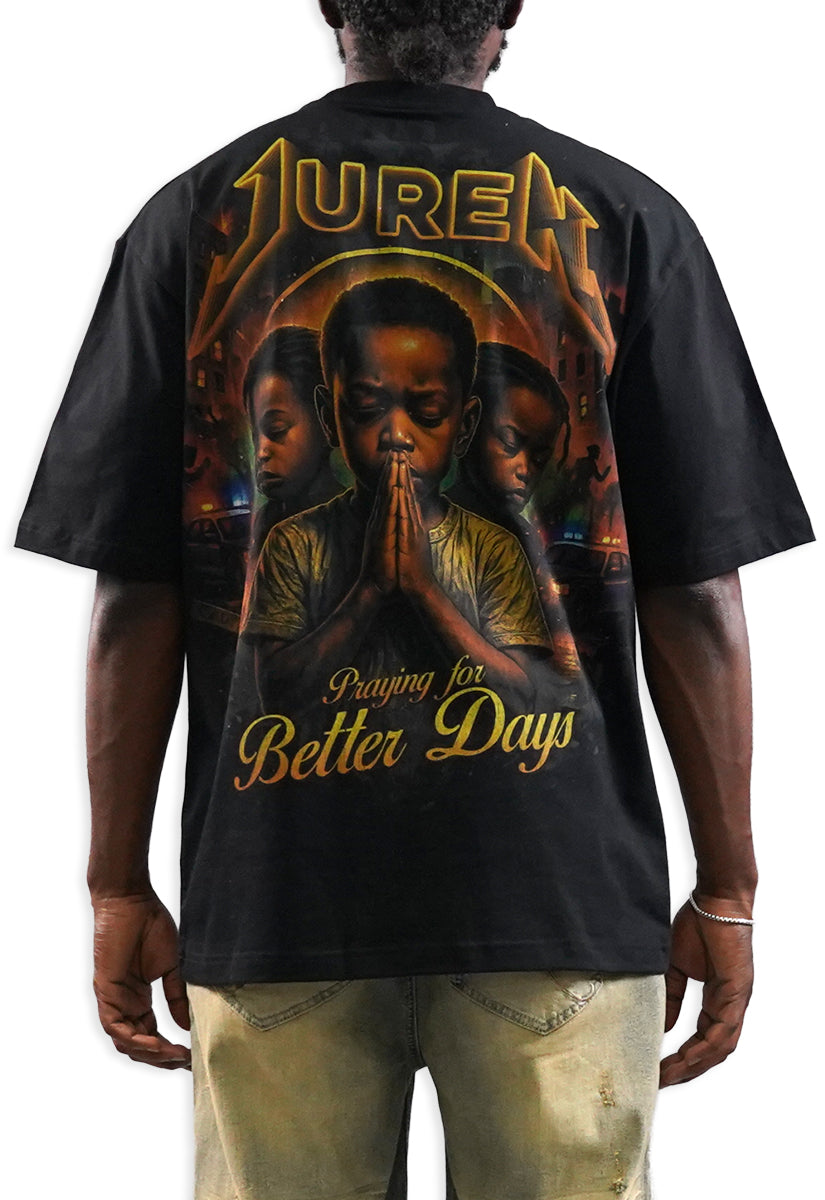 A man shown from the back wearing a black t-shirt with a large graphic print. The graphic features the word 'JUREN' in a gold metallic font at the top, a central portrait of a man in prayer, and the phrase 'Praying for Better Days' in gold at the bottom.
