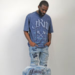 Man wearing a blue acid wash graphic t-shirt and jeans with a jacket on a plain background. Man wearing a blue acid wash t-shirt with text and graphics on the Juren logo battle axe