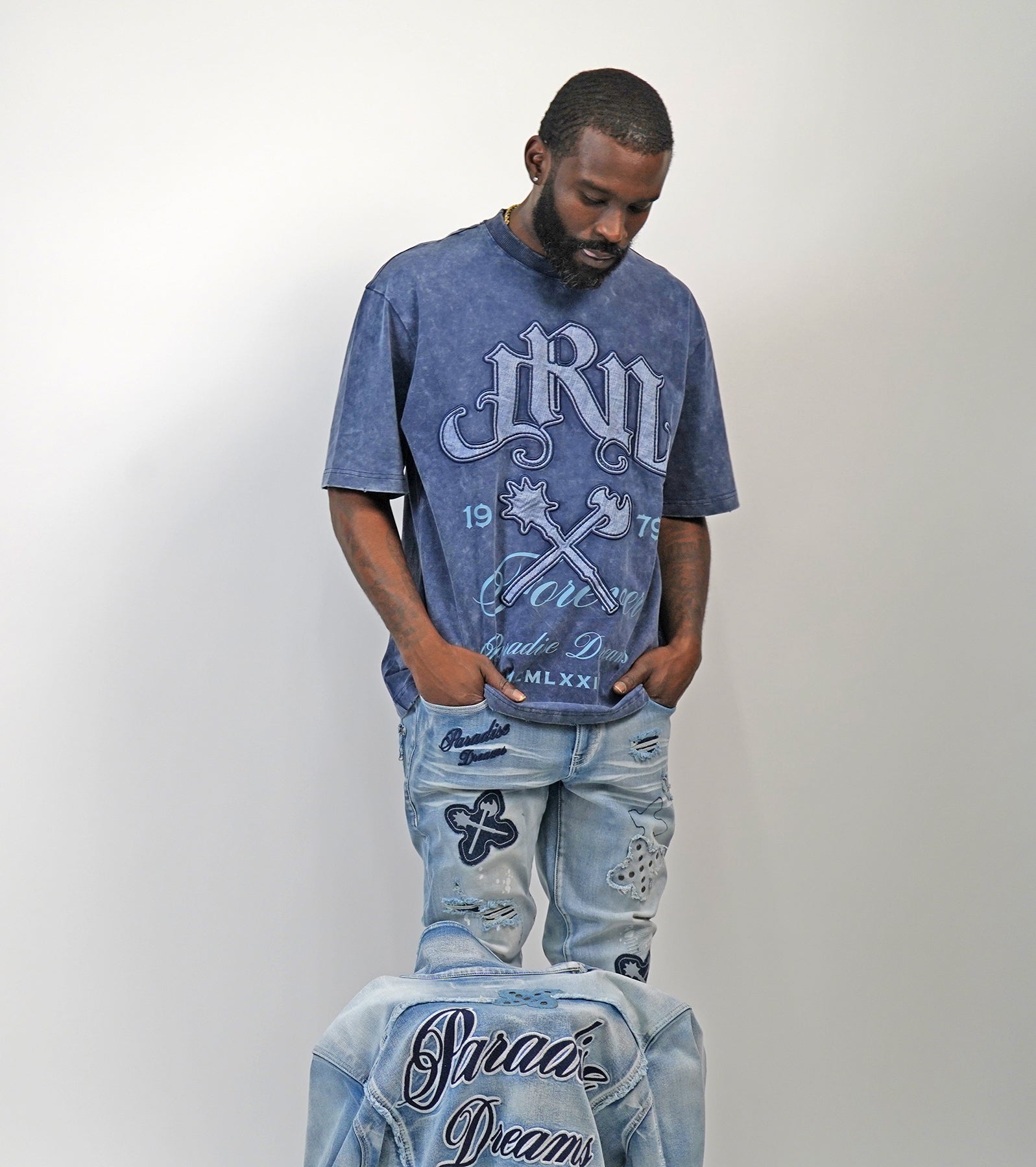 Man wearing a blue acid wash graphic t-shirt and jeans with a jacket on a plain background. Man wearing a blue acid wash t-shirt with text and graphics on the Juren logo battle axe