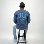 Person wearing a blue acid wash sweatshirt with text on the back, sitting on a black stool against a white background