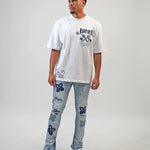 Person wearing a white t-shirt with text and graphics, paired with light blue jeans featuring floral patterns on a plain background. White t-shirt with navy text and graphics on a white shirt "Juren 1979 Logo.