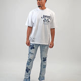 Person wearing a white t-shirt with text and graphics, paired with light blue jeans featuring floral patterns on a plain background. White t-shirt with navy text and graphics on a white shirt "Juren 1979 Logo.