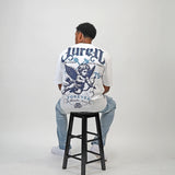 Person wearing a white t-shirt with Juren Logo on top with an Angel graphics and text, sitting on a black stool against a plain background