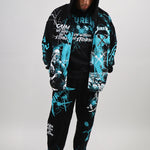 Person wearing a black and teal graphic hoodie and pants set on a white background