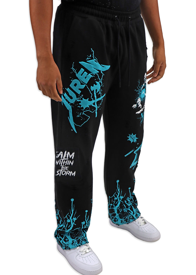 Black sweatpants with teal graphics and text worn by a person on a white background